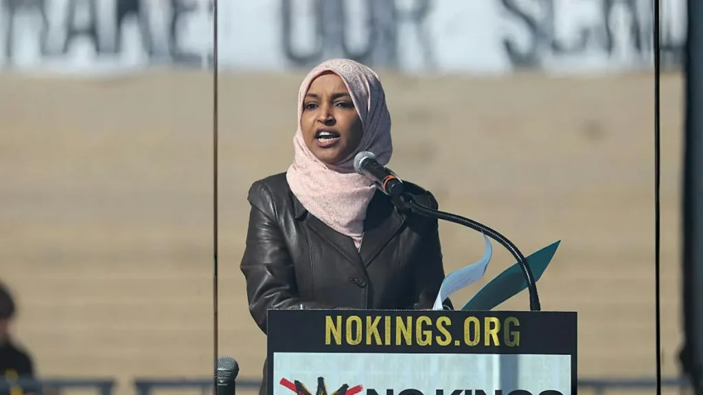 A woman wearing a hijab speaks at a podium with a sign that reads "NOKINGS.ORG."