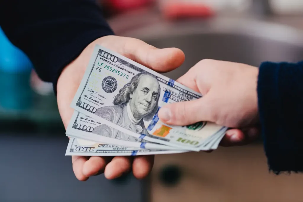 A person is holding a stack of $100 bills in their hands.