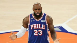 A basketball player wearing a Philadelphia 76ers jersey with the number 23 celebrates on the court.