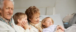 A family of four, including grandparents and grandchildren, is relaxing together on a couch.