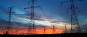 The image shows a silhouette of power transmission towers against a vibrant sunset sky, symbolizing the intersection of technology and nature.