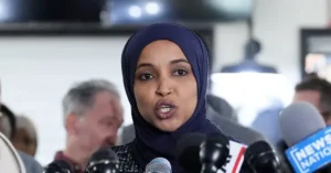A woman wearing a hijab speaks into microphones at a press conference.