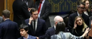 A man in a suit is seen on a phone call amidst a group of people in a formal setting.