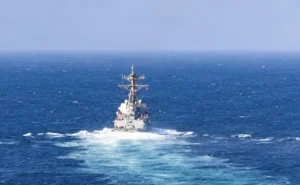 A naval ship is seen sailing through the open ocean under a clear sky.