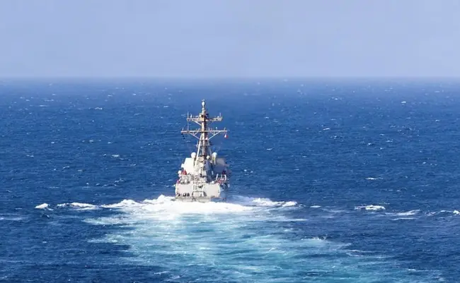 A naval ship is seen sailing through the open ocean under a clear sky.