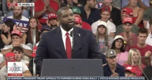 A man in a suit stands at a podium addressing a crowd at a rally in Fort Myers, Florida.