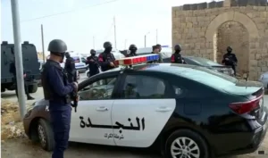 A group of police officers in riot gear stand near a police car marked "النجد" (The Rescue) in a desert-like setting.