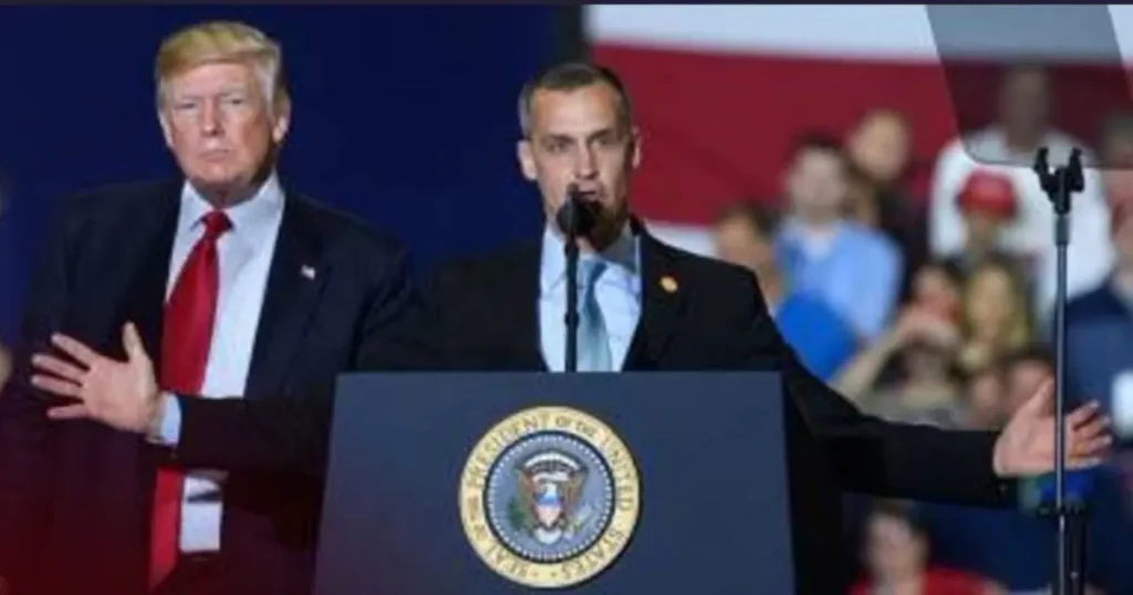 The image shows a political event with a man at a podium and another man standing beside him, both addressing an audience.