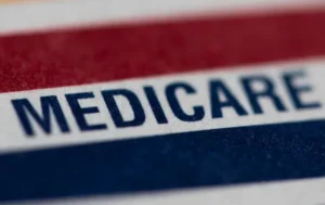 The image shows a close-up of a Medicare card with a red, white, and blue design.