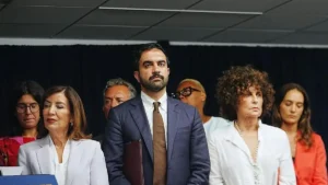 A group of individuals, including a man in a suit, stand together in a formal setting, possibly at a press conference or official event.
