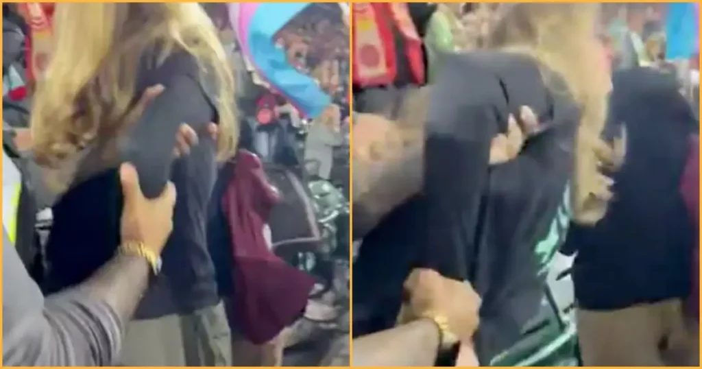 The image shows a person being restrained by others in a crowded setting, possibly during a protest or public event.