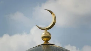 A golden crescent moon adorns the top of a dome, symbolizing Islamic architecture against a backdrop of a partly cloudy sky.