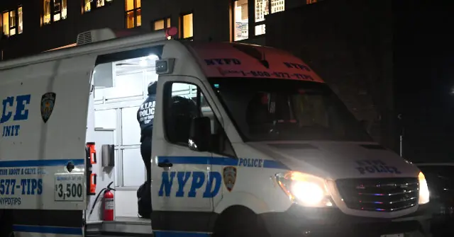 An NYPD police van is parked outside a building at night, with a person standing inside the van.