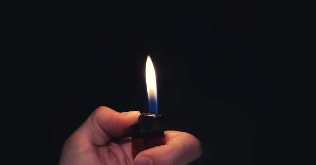 A hand holds a lit lighter against a dark background.