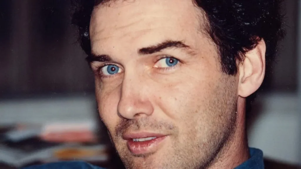 The image shows a close-up of a person with short, dark hair and a light complexion, wearing a blue shirt.