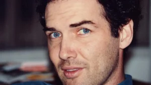 The image shows a close-up of a person with short, dark hair and a light complexion, wearing a blue shirt.