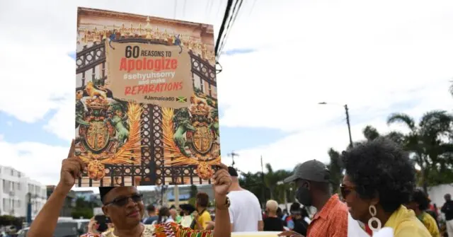 A protestor holds a sign advocating for "60 Reasons to Apologize and Reparations" in Jamaica.