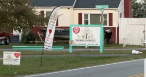 The image shows a sign for the "Thrive Learning Center East" located at 3118 Cofer Road, with additional smaller signs and a house in the background.