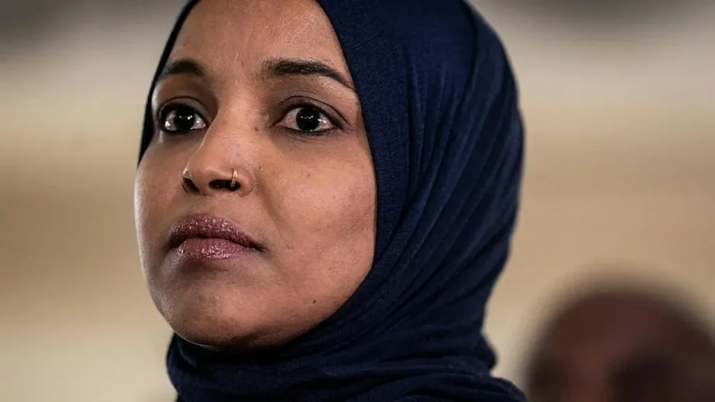 The image shows a person wearing a dark blue hijab, looking off to the side with a thoughtful expression.