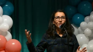 A woman is speaking into a microphone at an event decorated with balloons.