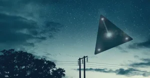 A triangular UFO hovers in the night sky above a power line and tree.