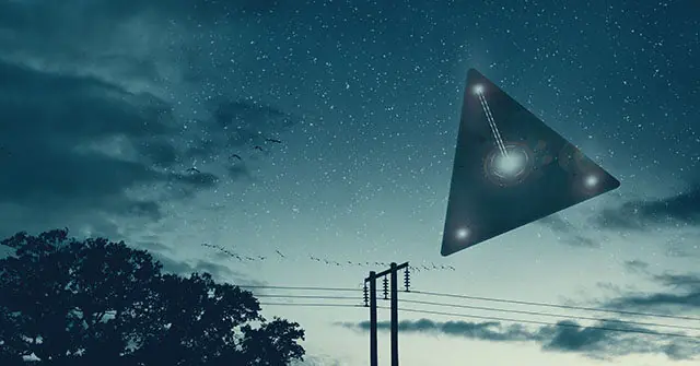 A triangular UFO hovers in the night sky above a power line and tree.