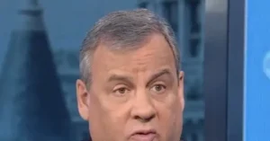 The image shows a close-up of a man with short gray hair, appearing to be in a news broadcast setting.