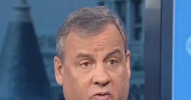 The image shows a close-up of a man with short gray hair, appearing to be in a news broadcast setting.