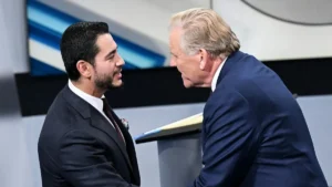 Two men in suits are engaged in a conversation on a stage with a modern background.