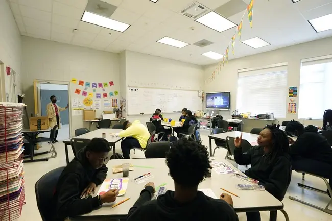 A classroom scene shows students engaged in art activities at their desks while a teacher stands at the front, leading a lesson.