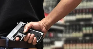 A person is holding a handgun in a holster, with a blurred background of what appears to be a store or display area.