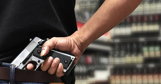 A person is holding a handgun in a holster, with a blurred background of what appears to be a store or display area.
