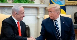 The image shows two men in formal attire shaking hands in a formal setting, likely a diplomatic or political meeting.