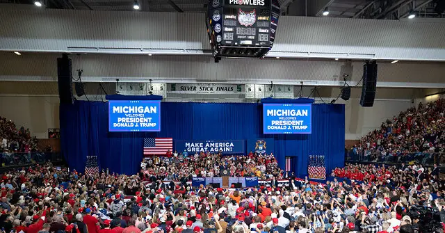 The photo shows a large rally in Michigan welcoming President Donald J. Trump, with a crowd gathered in a gymnasium.