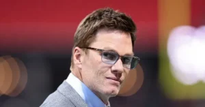 The image shows a man wearing glasses and a suit, with a blurred background featuring colorful bokeh lights.