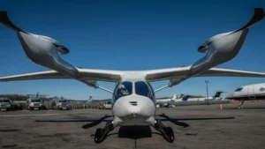 The image shows a futuristic-looking aircraft with a unique design, featuring large, swept-back wings and a sleek, modern body, parked on an airport tarmac.
