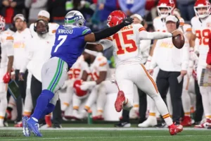 A football player in a blue jersey attempts to block a pass from a player in a white jersey during a game.