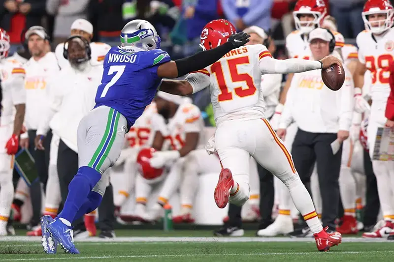 A football player in a blue jersey attempts to block a pass from a player in a white jersey during a game.