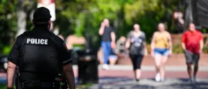 A police officer stands in the foreground as pedestrians walk in the background on a sunny day.