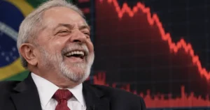 The image shows a man in a suit and tie, smiling, with a Brazilian flag and a red downward trend line in the background, suggesting a discussion about economic or political matters.