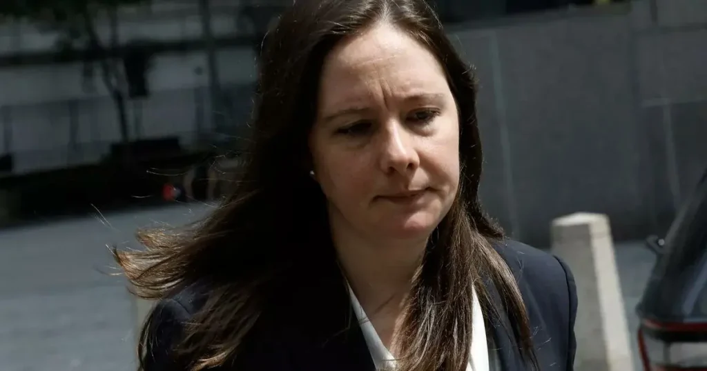 The image shows a woman with long hair, wearing a dark blazer, walking outdoors with a serious expression.