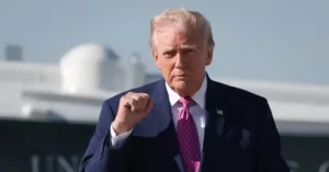 The image shows a person in a suit and tie, standing in front of a large aircraft, with a serious expression and a fist raised.