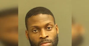 The image is a mugshot of a man with short hair and a beard, captured in a formal police setting.