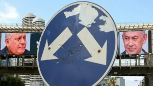 A weathered road sign with two arrows pointing in opposite directions is set against a backdrop of political campaign billboards featuring two prominent figures.