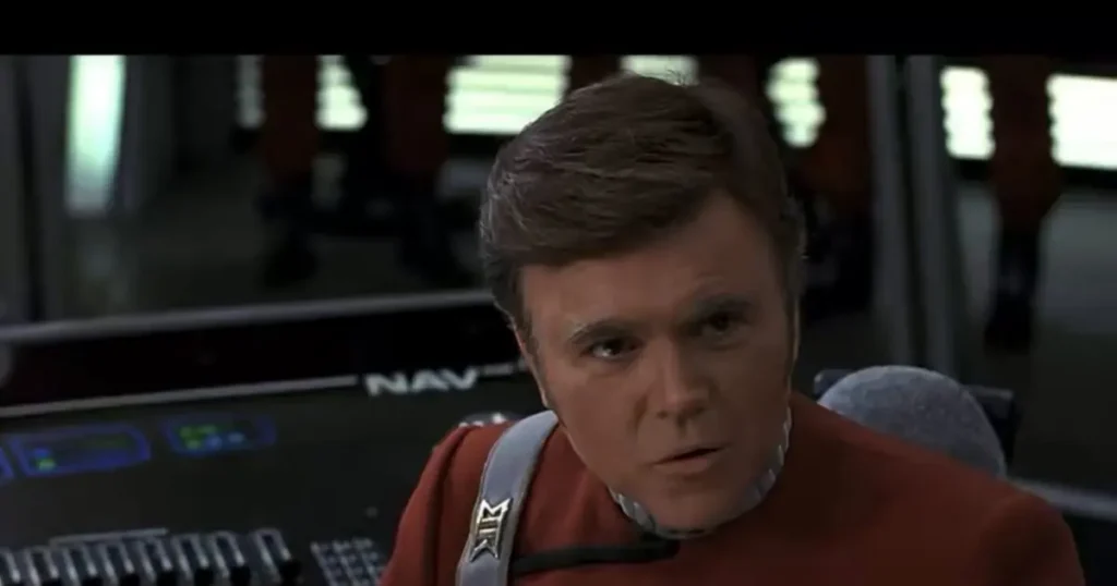 The image shows a person in a red uniform with a harness, seated in a control room with a "NAV" panel in the background.