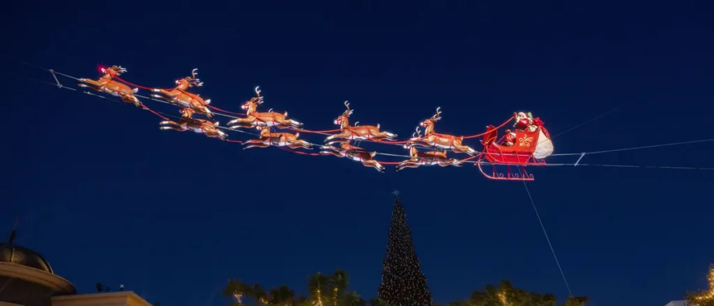 A festive Christmas scene featuring Santa Claus in his sleigh being pulled by reindeer against a dark blue sky.