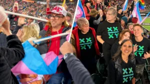 A group of people celebrate and wave flags at a lively event, with some wearing shirts featuring a green and blue logo.