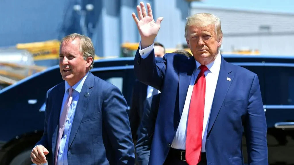 The image shows a man in a blue suit and red tie waving, accompanied by another man in a blue suit and pink tie, as they appear to be disembarking from an aircraft.