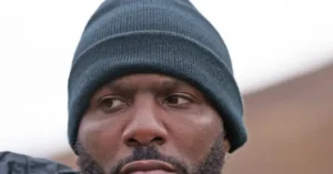 The image shows a close-up of a person wearing a dark beanie, looking off to the side with a thoughtful expression.