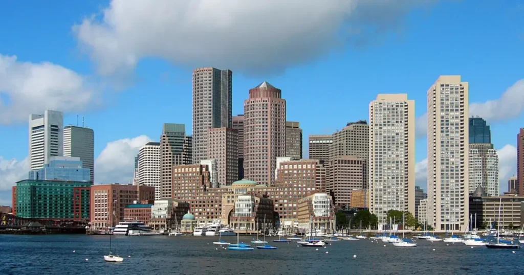 The image showcases a vibrant cityscape with a mix of modern high-rise buildings and historic architecture, set against a backdrop of a clear blue sky with scattered clouds, and a marina filled with boats in the foreground.
